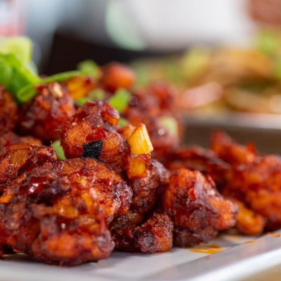 Close-up of spicy fried meatballs garnished with chopped green onions and peppers on a rectangular serving plate.