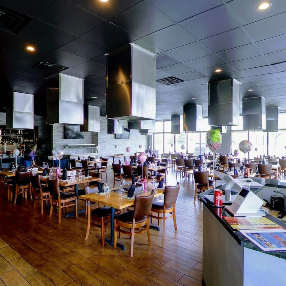 Spacious modern restaurant dining room with wooden tables, leather chairs, pendant lights, colorful balloons, and bright windows.
