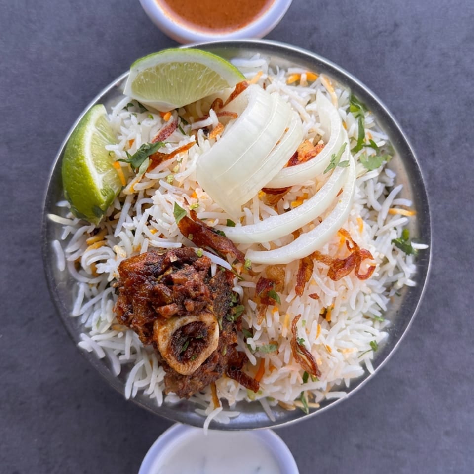 Overhead view of spiced basmati rice topped with roasted meat, fried onions, cilantro, lime wedges, and sauce.