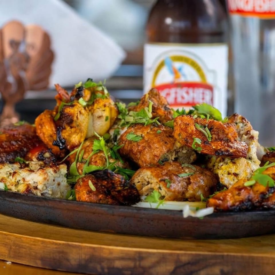 Assortment of grilled, spiced kebabs garnished with fresh herbs on a black platter atop a wooden serving board.